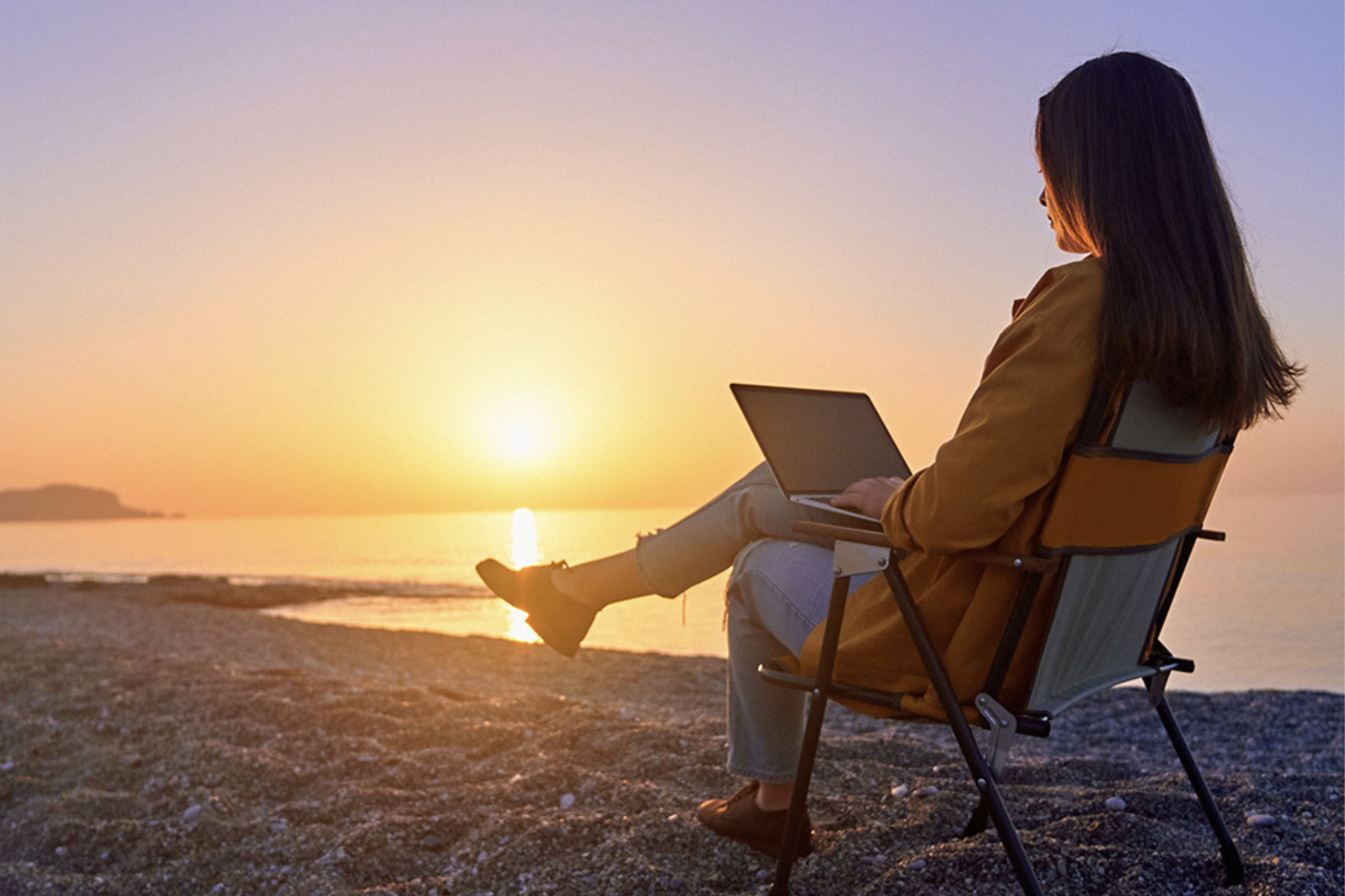 Woman watching the Catholic Mass online on her laptop with a sunset in the background